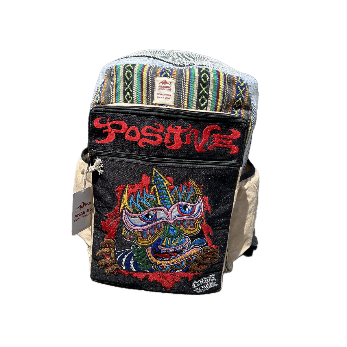 Akashic Connections × Chris Dyer “Positive” hemp backpack with a trippy striped top, vibrant multicolored creature patch, bold red “POSITIVE” text, and side brand tag, displayed against a white background.