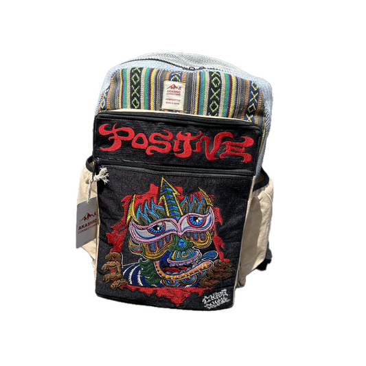 Akashic Connections × Chris Dyer “Positive” hemp backpack with a trippy striped top, vibrant multicolored creature patch, bold red “POSITIVE” text, and side brand tag, displayed against a white background.