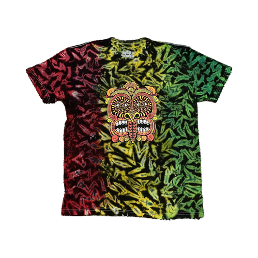 The Rainbow/Rasta Tribal Mask 2023 Tie Dye T Shirt with bold red, yellow, and green tie-dye and a large psychedelic Maori mask design lies flat on a black-and-white patterned rug.