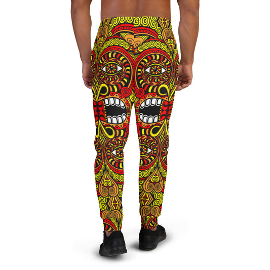 A shirtless person faces away, wearing Tribal Love joggers with a bold tribal pattern in yellow, red, and black and large stylized face designs. Black shoes complete the outfit.